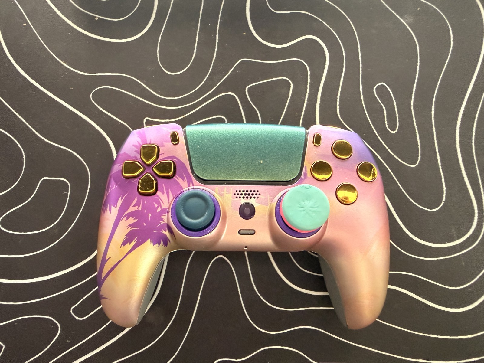 My custom PS5 controller with a sunset-and-palm-tree front plate, teal touchpad, and gold buttons